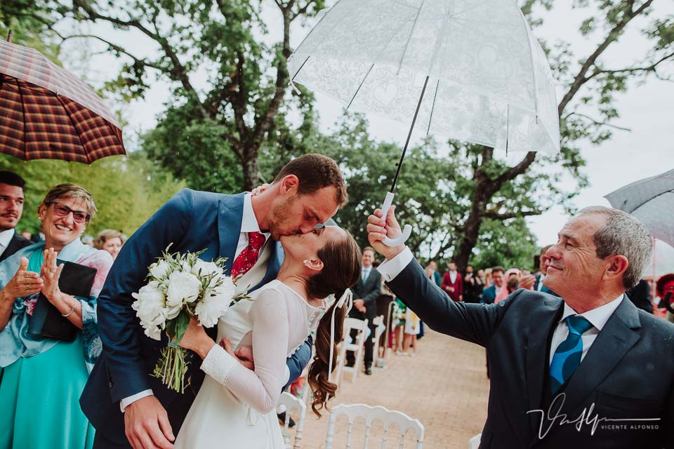 Novio besando a la novia bajo la lluvia después de casarse