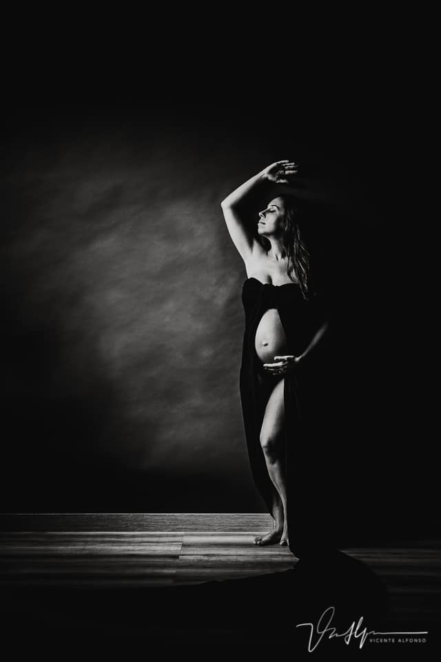 Perfil plano general de embarazada en estudio pegada a la pared en blanco y negro