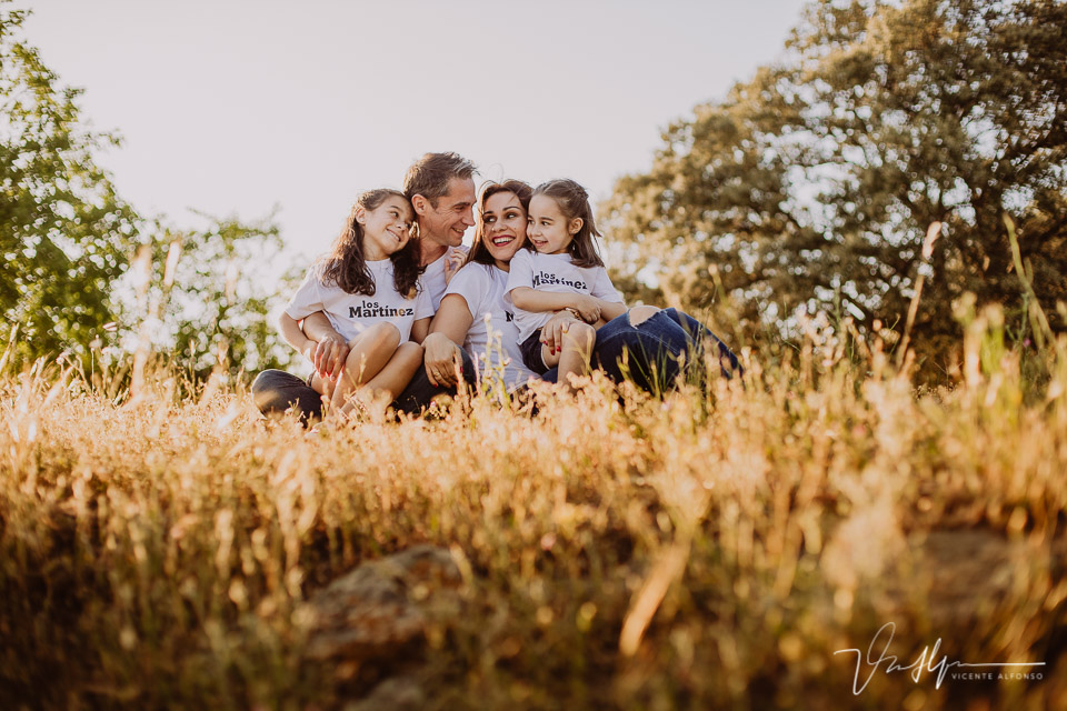 Familia de cuatro personas sonriendo sentadas en el campo entre espigas