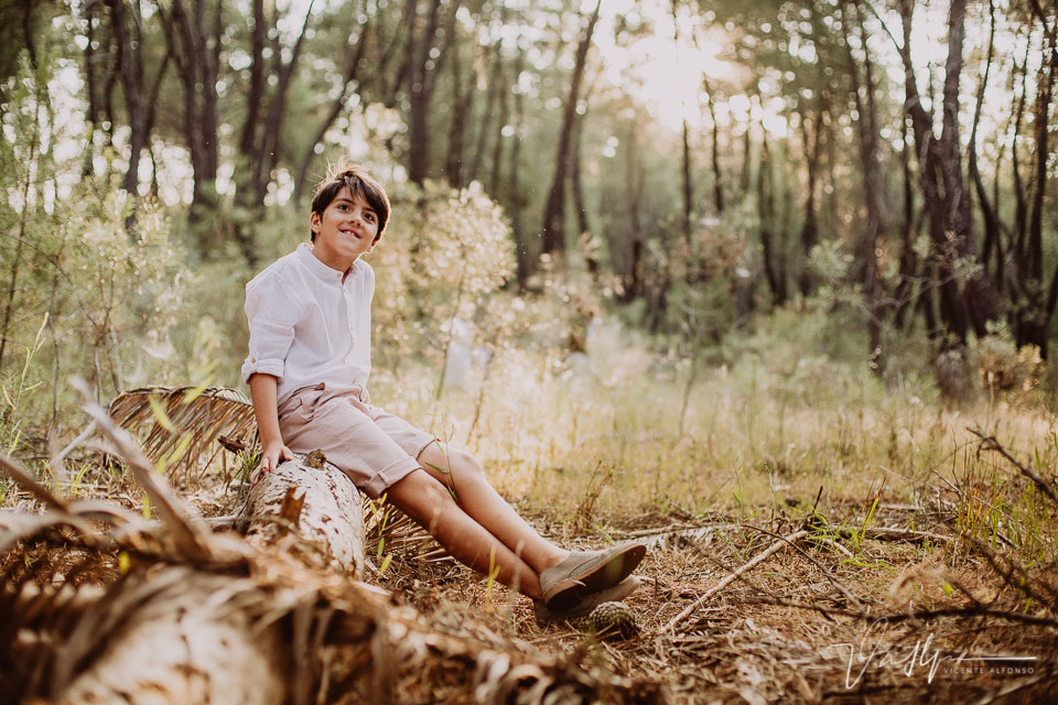 Niño sentado en un tronco en mitad del campo